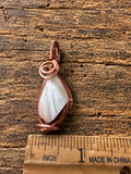 Copper wire-wrapped moonstone pendant next to ruler showing size