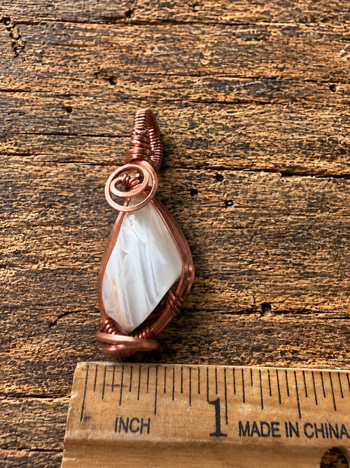 Copper wire-wrapped moonstone pendant next to ruler showing size