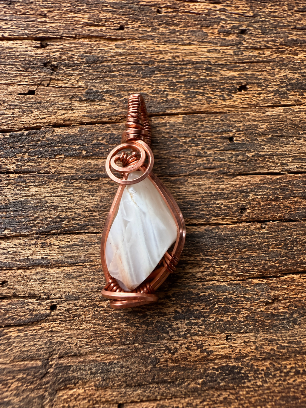 Back view of copper wire-wrapped moonstone pendant on wood surface